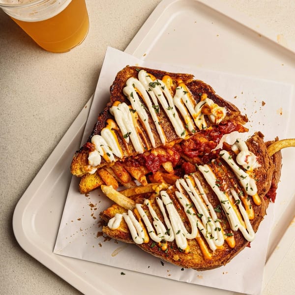 A grilled cheese sandwich with fries, red sauce, white sauce, and parsley, next to a beer.
