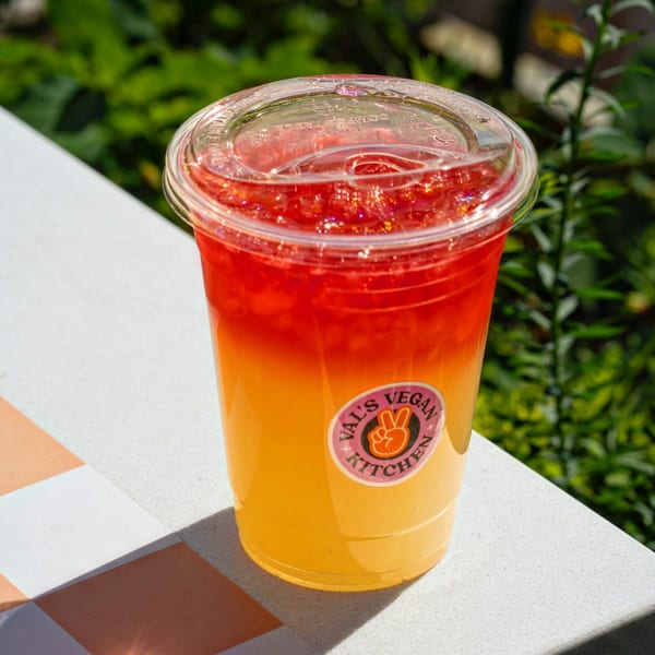 A Val's Vegan Kitchen drink, red on top and yellow on the bottom, sits on a tiled surface.