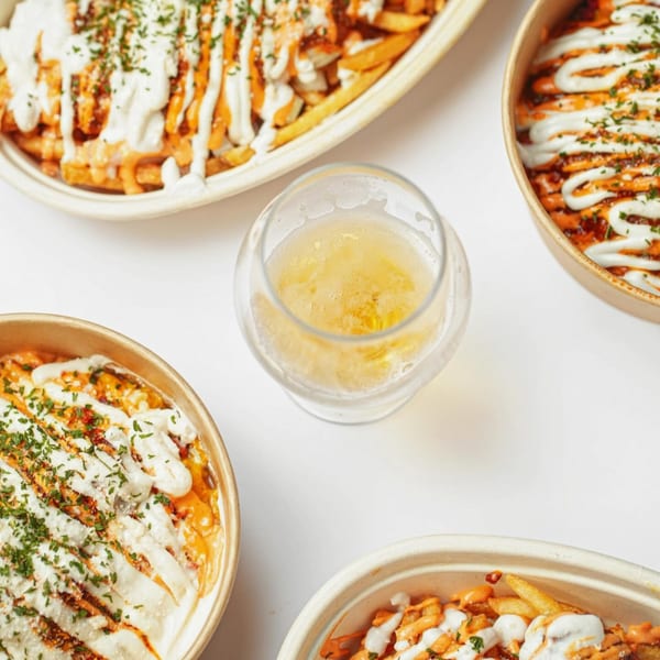 Four bowls of loaded fries with various sauces and herbs, surrounding a glass of beer.