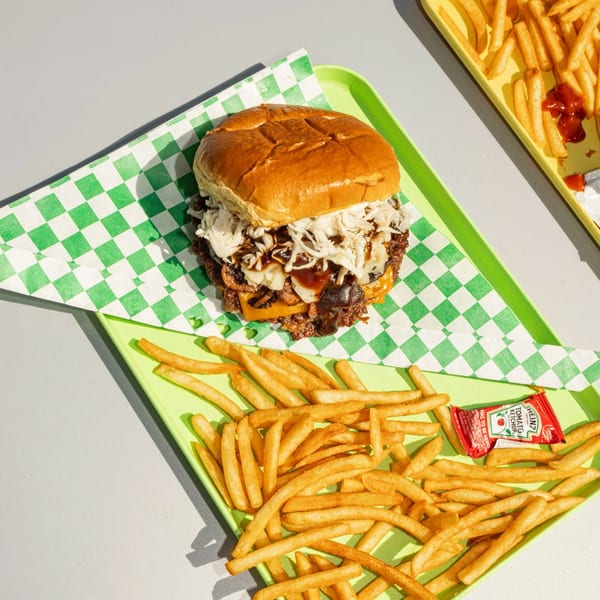 A burger with cheese, onions, and sauce on a green checkered wrapper, with fries and ketchup.